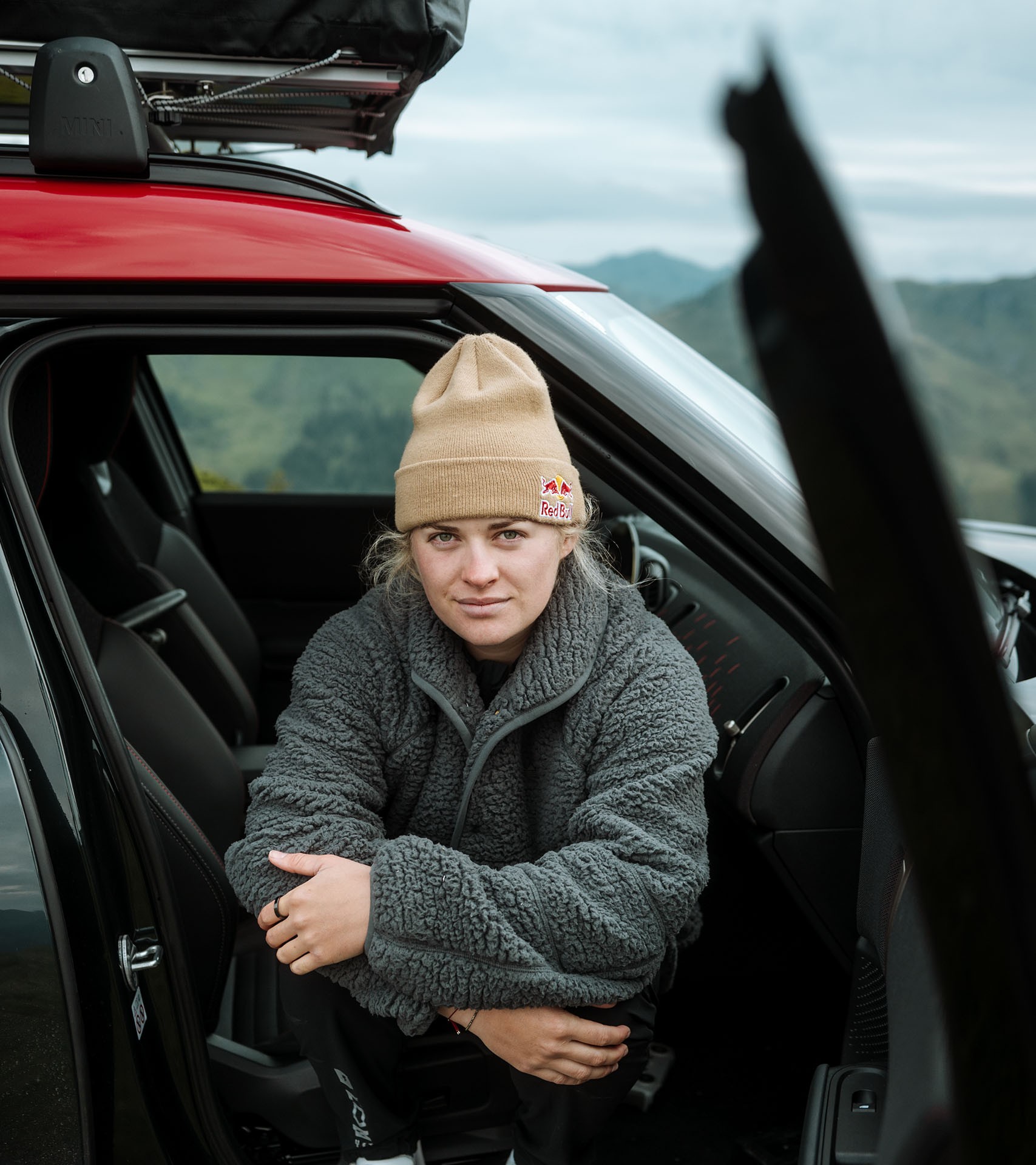 Wearing a grey fleece jumper and beige beanie, Vali Höll poses for a photo from the open passenger side of the new MINI John Cooper Works Countryman.